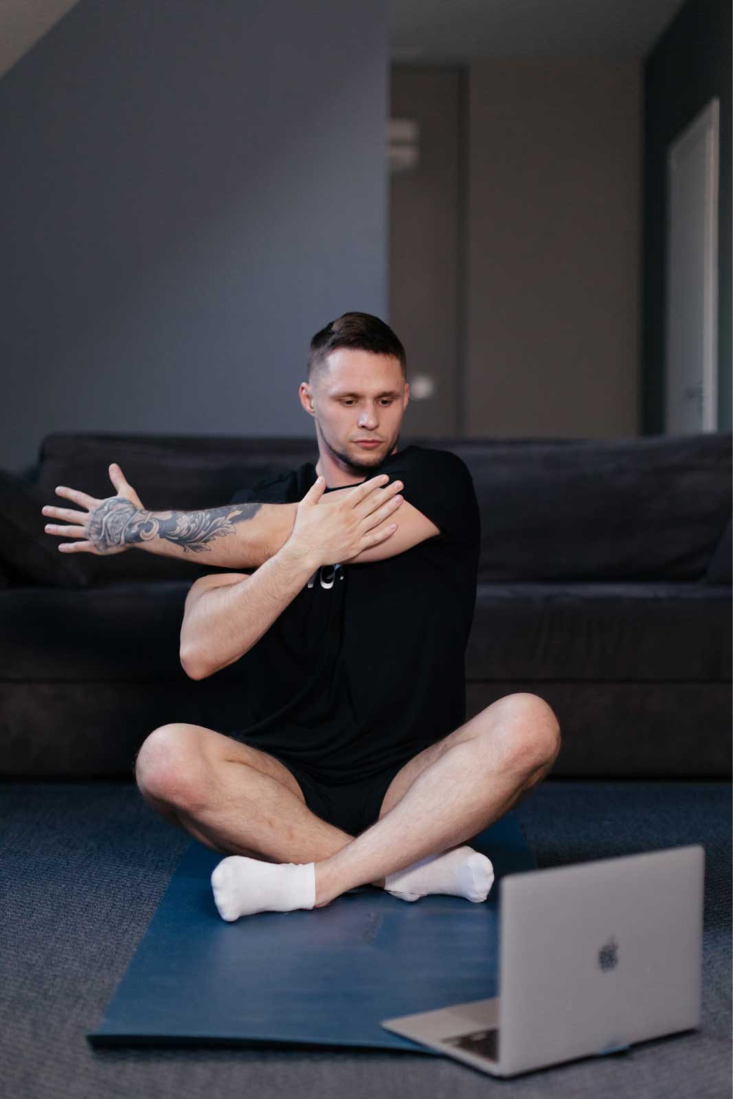 Man sitting cross-legged on a mat in front of a laptop