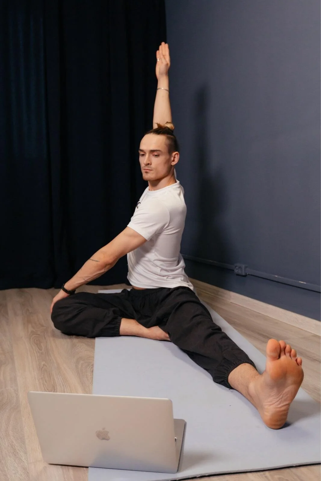 Man doing a seated stretch on a mat in front of a laptop during an online session